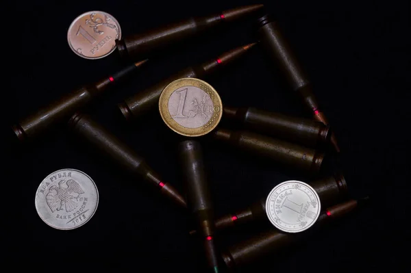 黒を背景にライフル銃の軍事的弾薬を持つ1ユーロ 1つのロシアルーブルとウクライナのフリフナ硬貨 お金のための戦争を象徴する 世界最大の問題 — ストック写真