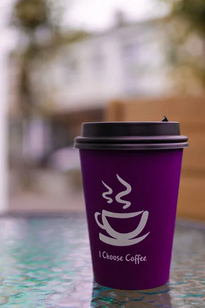 Purple-pink coffee paper cup on glass clear table. On cup wrote: \