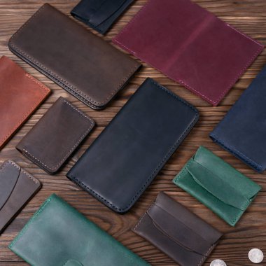 Ahşap desenli arka planda diğer deri aksesuarlarla çevrili siyah renkli deri porte-monnaie. Yan görüş. Lüks aksesuarların stok fotoğrafı.