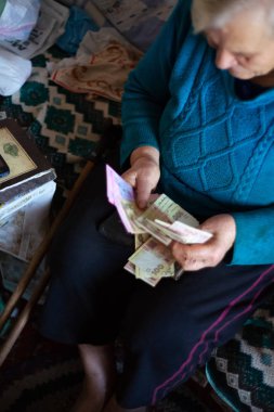 Ukrayna, Kiev, Aralık 12 2018. Eski zavallı gri saç kadın elinde Ukrayna Grivnası para tutar. Kadın üzücü. Köyde kötü hayat. Yaşlılık iyi değil. Düşük hafif fotoğraf. Yalnızca editoryal kullanım.