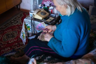 Ukrayna, Kiev, Aralık 12 2018. Eski zavallı gri saçlı kadın elinde Ukraynalı kağıt para tutar. Kadın üzücü. Köyde kötü hayat. Yaşlılık iyi değil. Düşük hafif fotoğraf. Yalnızca editoryal kullanım.