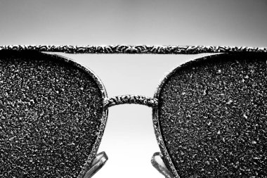 Sunglasses with artificial snow on white-purple background close-up view. Monochome black and white image. clipart