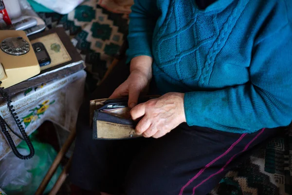 Yaşlı, gri saçlı kadın Ukrayna 'nın Hryvna parasını elinde tutuyor. Kadın üzgün. Köyde fakir bir hayat. Yaşlılık iyi değil. Düşük ışık fotoğrafı.