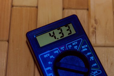 Ahşap zeminde mavi dijital çokölçer. 4.33V veya tam şarjlı pil gösteriyor. Voltmetre, ampermetre, ohmmetre içerir.