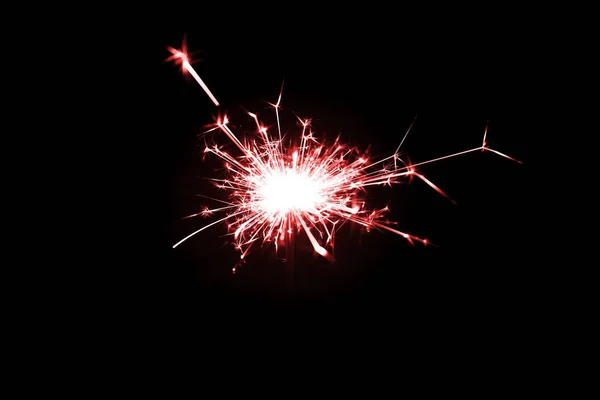 Low light photo of bengali fire isolated on black background with red toning. A lot of light and sparks. Underexposed photo.