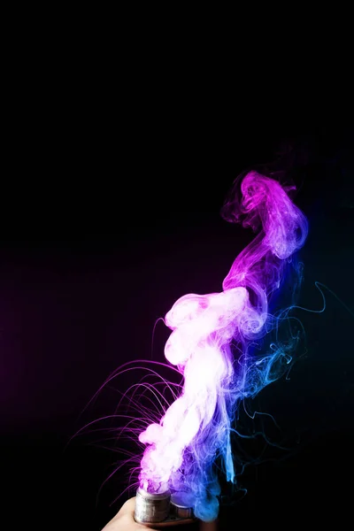 Чоловіча рука тримає вейп у густому тумані або диму. Вейп-хмари навколо руки з вейпом на чорному тлі. Туман подвійного кольору синій і фіолетовий. Запас ізольований барвистий дим з розпилювачем гліцерин . — стокове фото