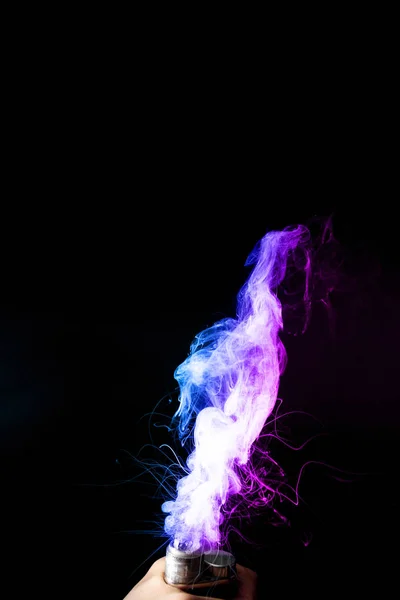 A hím kéz sűrű gőzködben vagy füstben tartja a gőzt. Vape felhők körül kéz a kézben, gőz a fekete háttér. A köd kettős színű kék és lila. Készlet izolált színes füst spray glicerin. — Stock Fotó
