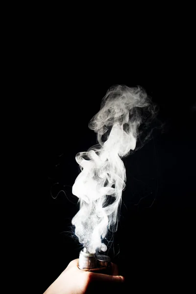 La mano del hombre sostiene el vapor. Vape nubes salpicaduras de la bobina en backg negro — Foto de Stock