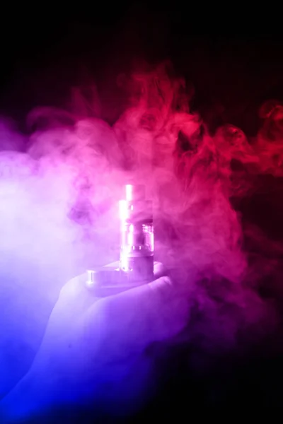 Male hand holds vape in thick vape fog or smoke. Vape clouds around hand with vape on black background. Fog is dual color  blue and purple. Stock isolated colorful smoke with spray glycerine. — Stock Photo, Image