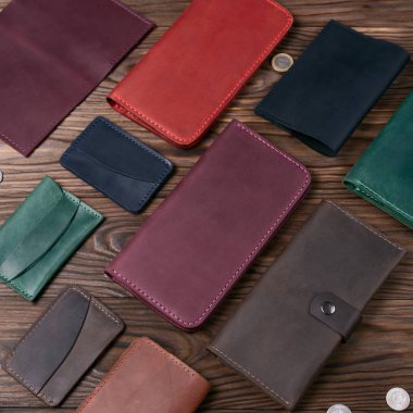 Ahşap desenli arka planda diğer deri aksesuarlarla çevrili mor renkli el yapımı deri porte-monnaie. Yan görüş. Lüks aksesuarların stok fotoğrafı.