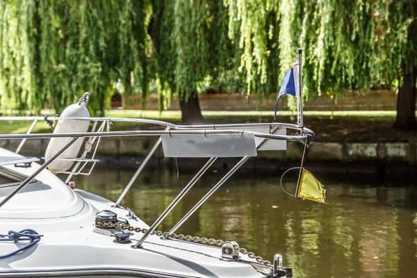 Part of a small yacht in small a river with some trees in the background