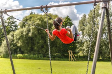Bir kız huzur içinde güzel bir yeşil park içinde büyük bir salıncak üzerinde sallanır.