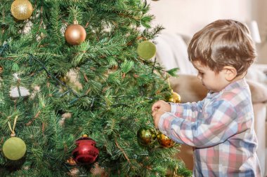 Güzel bir sarışın çocuk evinin oturma odasında Noel ağacı üzerinde dekoratif objeler koyar
