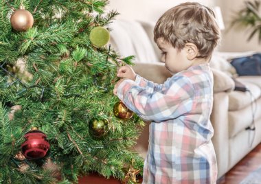 Küçük bir çocuk Noel ağacında renkli topları yerleştirir