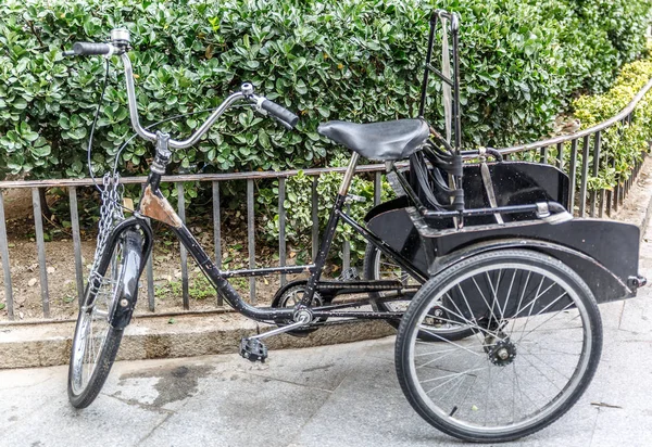 Black bicycle with three wheels attached to a small metal fence.