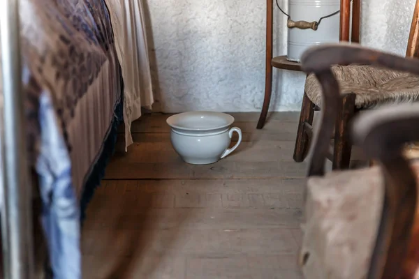 Eski bir evde bir yatak odasında bir yatak yanına yerleştirilmiş eski beyaz pisuvar
