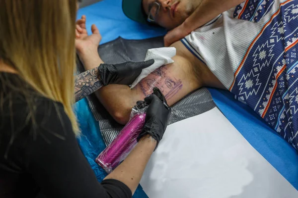 A tattooist woman cleans the tattoo she is doing to a boy on his