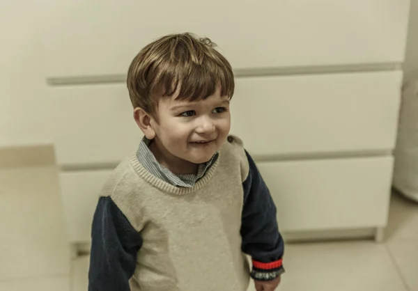 Un niño vestido con un suéter sonríe mientras está en su habitación —  Fotos de Stock