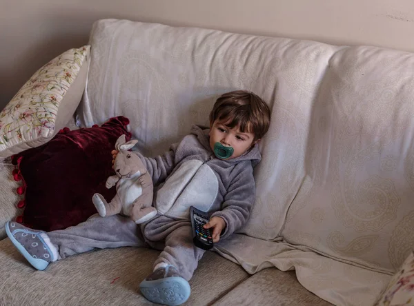 Маленький хлопчик у піжамі сидить на дивані у вітальні з — стокове фото