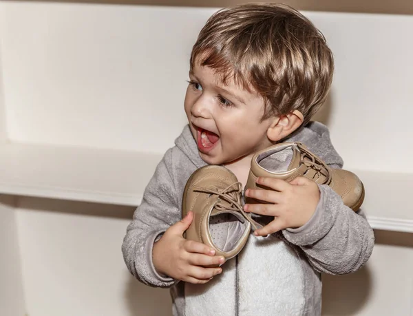一个可爱的小男孩一边微笑一边拿着他的小鞋 — 图库照片