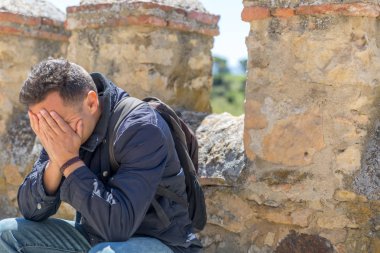 Yüzünde elleri ile ceket ve sırt çantası ile Sad adam, oturma