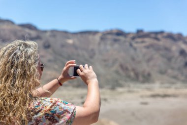 Olgun bir sarışın turist bir çöl ve volca fotoğraf çekiyor
