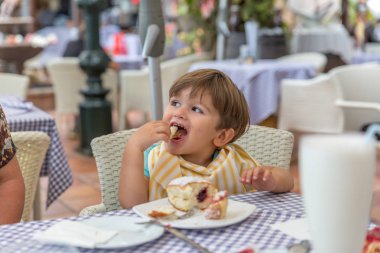 O bir co pasta büyük bir parça yiyor gibi sevimli bir sarışın çocuk gülümsüyor
