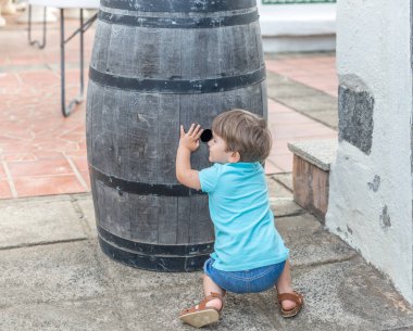Mavi oyunlar giymiş hoş bir çocuk bir varil arkasında gizlemek