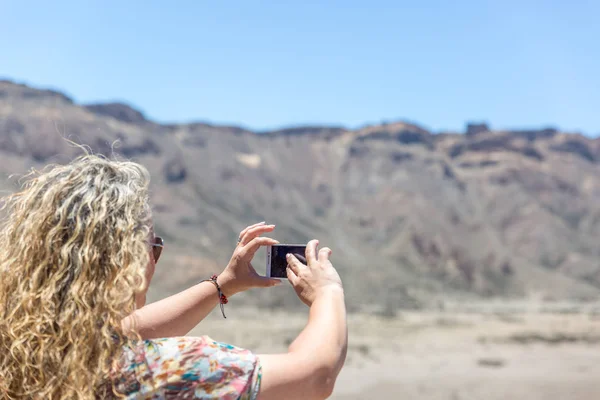 stock image A mature blonde tourist is taking pictures of a desert and volca