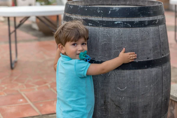 Un niño bonito vestido de azul con un chupete abraza un barril —  Fotos de Stock