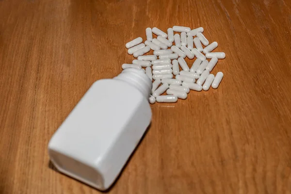Set of white pills coming out of a white canister on a brown sur — Stock Photo, Image