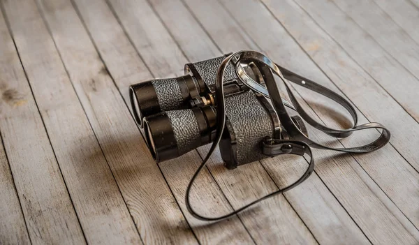 Small black binoculars isolated on a wooden surface — Stock Photo, Image