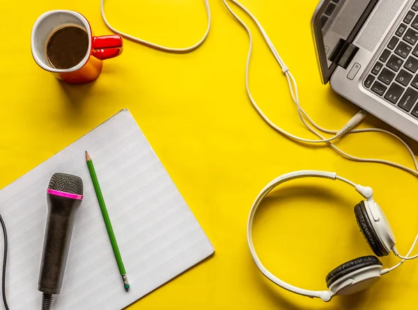 Set consisting of red coffee cup, music notebook, microphone, headphones, notebook and pencil on a yellow surface