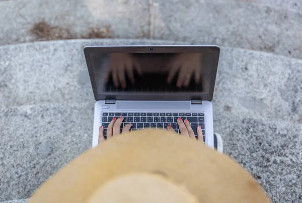 Vue d'en haut d'une fille avec un chapeau travaillant avec son ordinateur portable à l'extérieur . — Photo