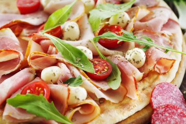 Pizza bir ahşap masa yakın çekim prosciutto jambon, mozzarella, domates ve çeşitli maddeler üzerinde.