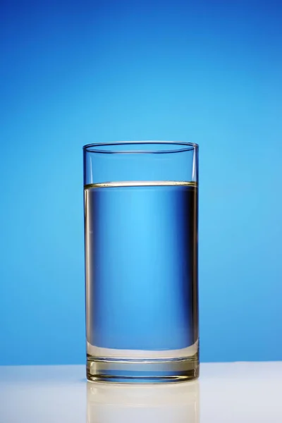 Een glas schoon water op een blauwe achtergrond. — Stockfoto
