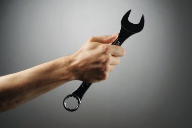 Erkek el gri bir arka plan üzerinde bir İngiliz anahtarı tutan.