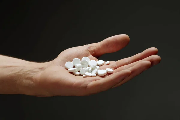 Eine Handvoll Tabletten in der männlichen Hand auf dunklem Hintergrund. Stockbild