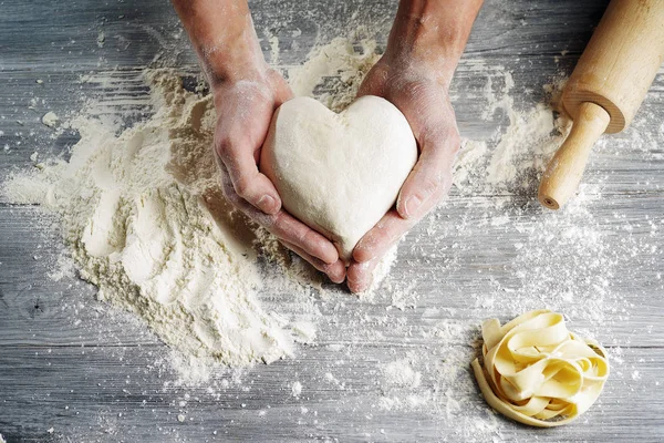 Teig in Herzform von Bäckerhänden in Großaufnahme gehalten. Stockbild