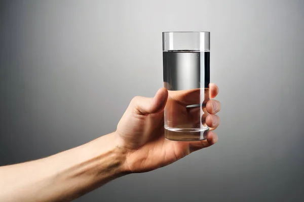 Een glas water houdt een hand tegen een grijze achtergrond. — Stockfoto