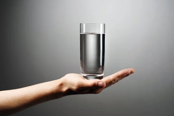 Een glas water houdt een hand tegen een grijze achtergrond. — Stockfoto