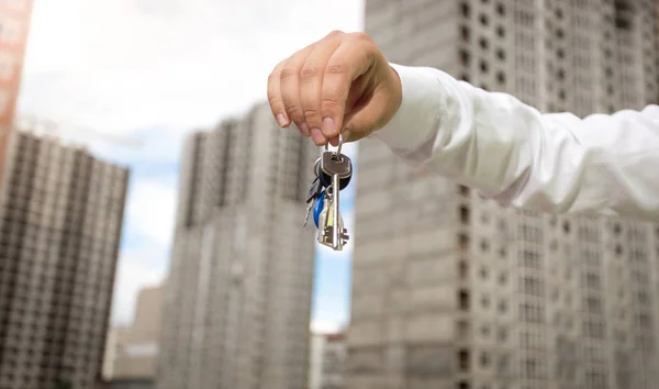 Närbild bild av manlig hand hålla nycklar från nya huset över backound av byggnadsplatsen — Stockfoto