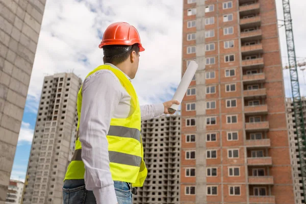 Trabalhador da construção masculino em hardhat segurando plantas e apontando para o edifício em construção — Fotografia de Stock