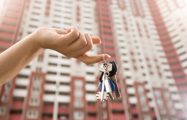 Closeup image of female hand holding keys from new house against big building