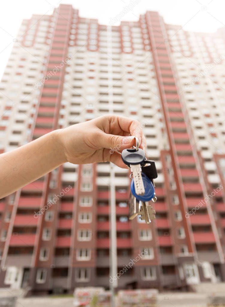 Closeup image of female hand holding keys from new apartment against big house under construction