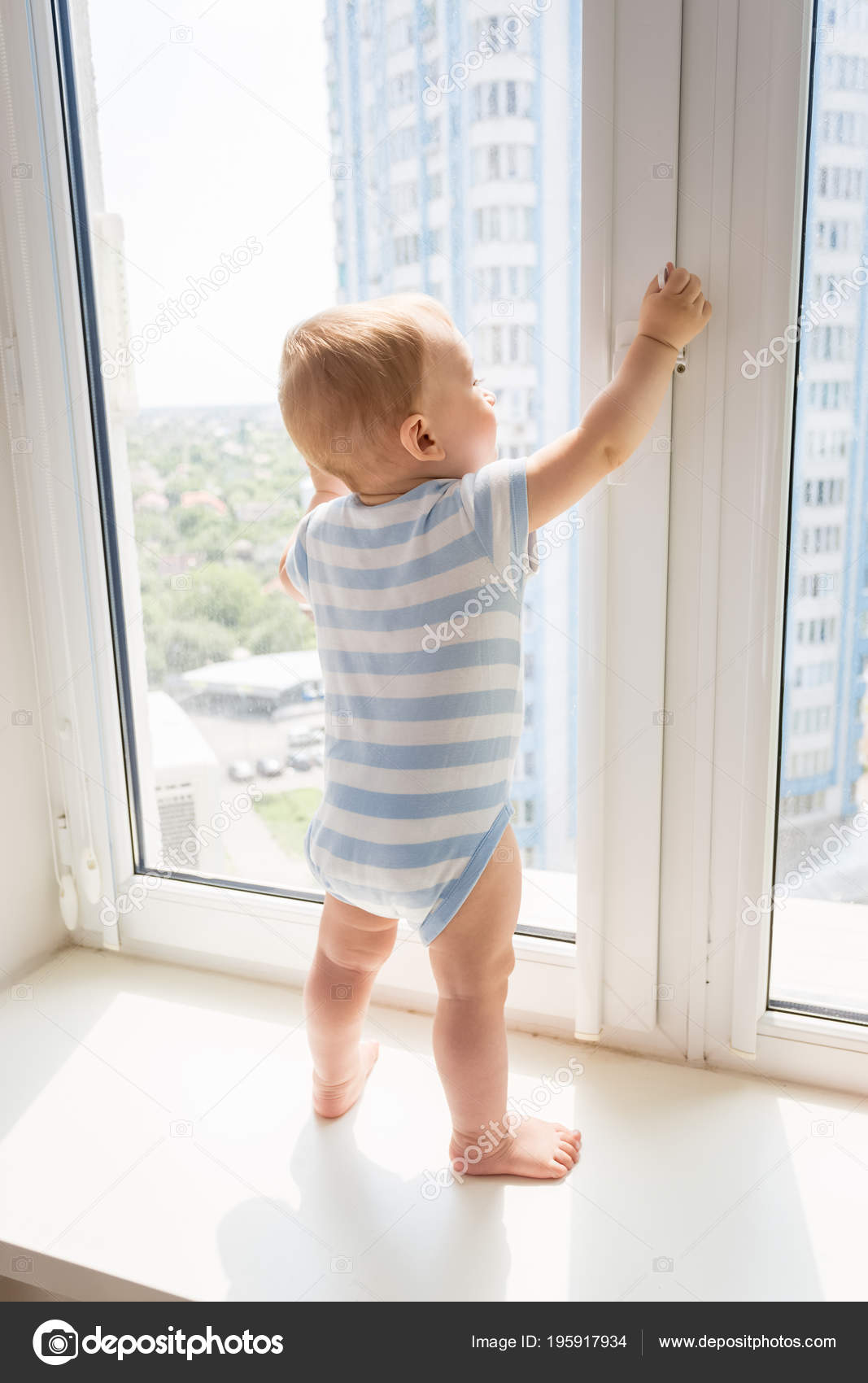 months old baby boy standing on windowsil and trying to open the