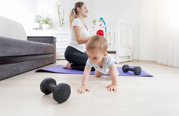 Adorable bebé niño arrastrándose en el suelo mientras su madre practicando fitness en casa — Foto de Stock