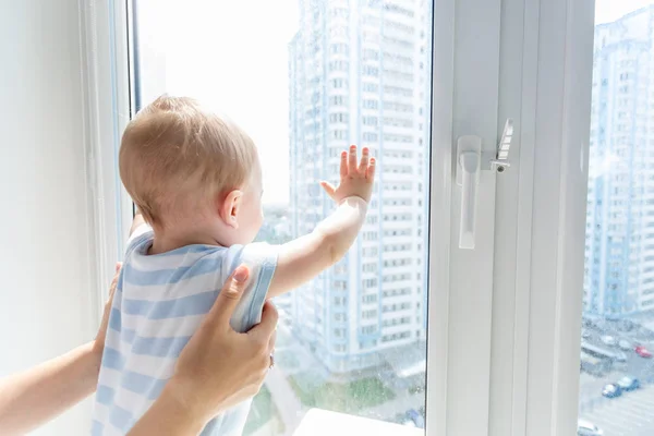 Zbliżenie obrazu rąk rodziców posiadających bbay chłopiec stoi na parapecie i patrząc z okna — Zdjęcie stockowe