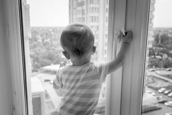 Imagem em preto e branco do bebê puxando a alça da janela e tentando abri-la — Fotografia de Stock