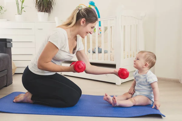 Foto tonificada de lindo niño sonriente mirando a la madre sentada en la alfombra de fitness y practicando fitness — Foto de Stock